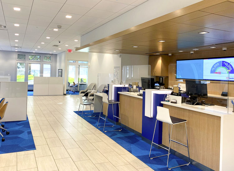 US Bank teller counter area featuring warm wood millwork, blue geometric carpet, and modern digital displays